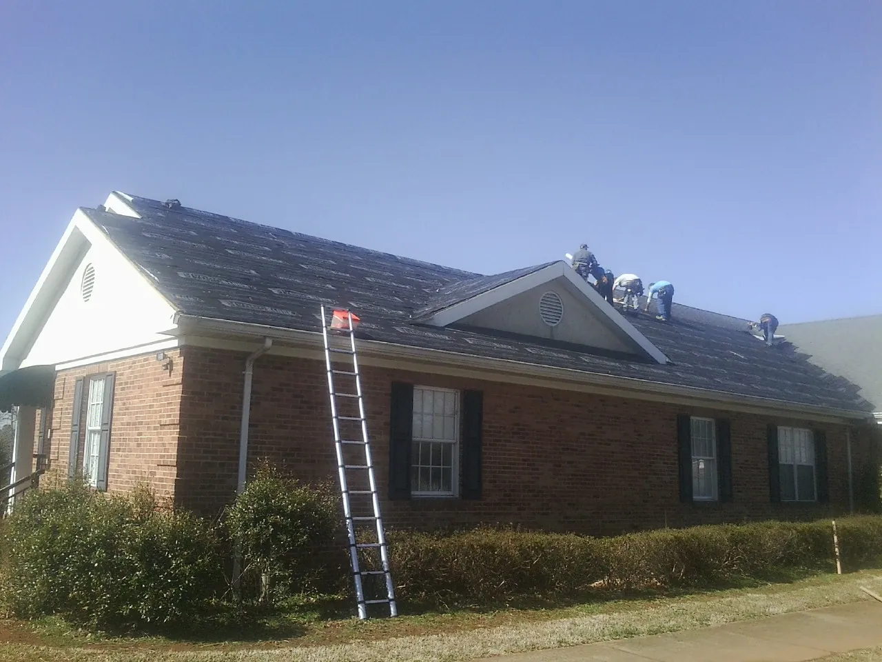 Crew tearing shingles off a brick ranch roof with a ladder set — Metal Roof Repair work by our crew in Yukon