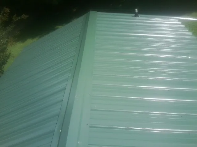 New green metal panels meeting at the ridge of a roof — Flat Roof Repair work by our crew in Yukon