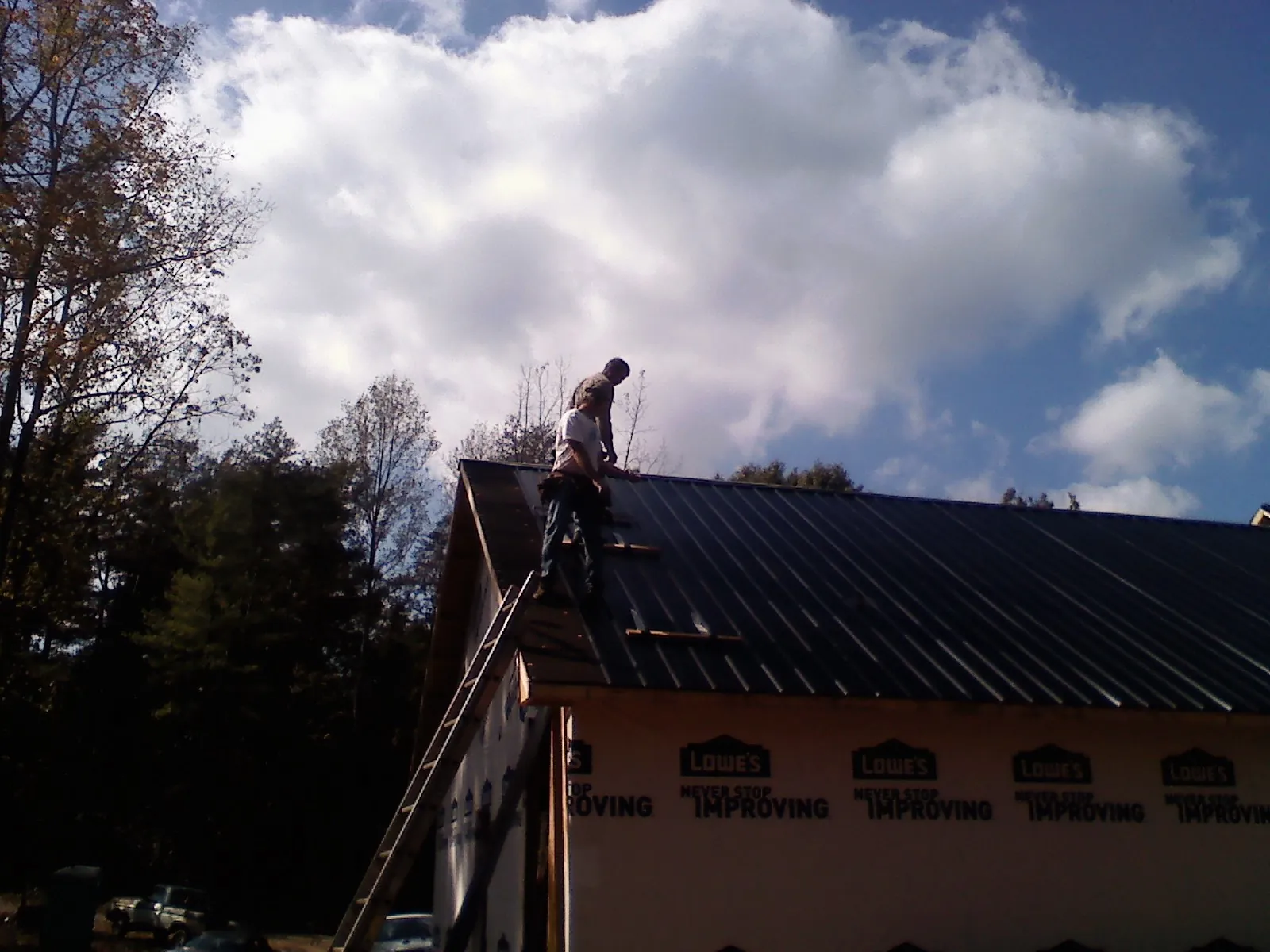 Roofer fastening dark metal panels high against a cloudy sky, from a Roof Inspection job in Yukon