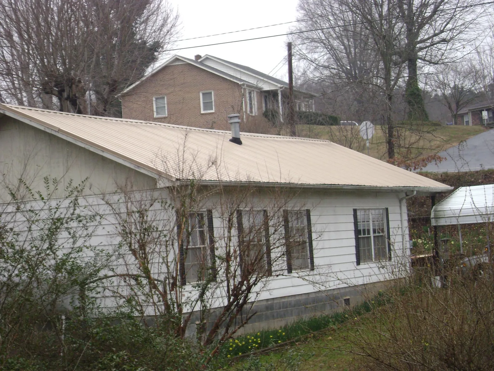 Tan metal roof on a white sided house set into a hillside — Commercial Roofing by Roofing Brothers in Yukon